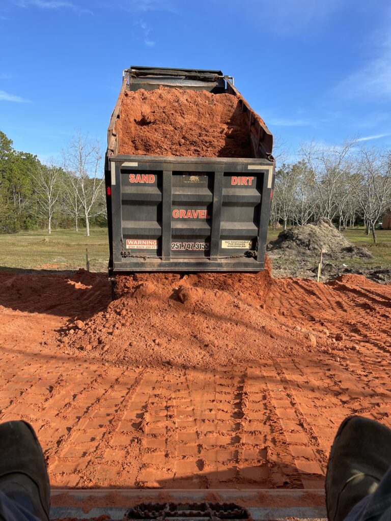 A dump truck unloading red fill dirt.